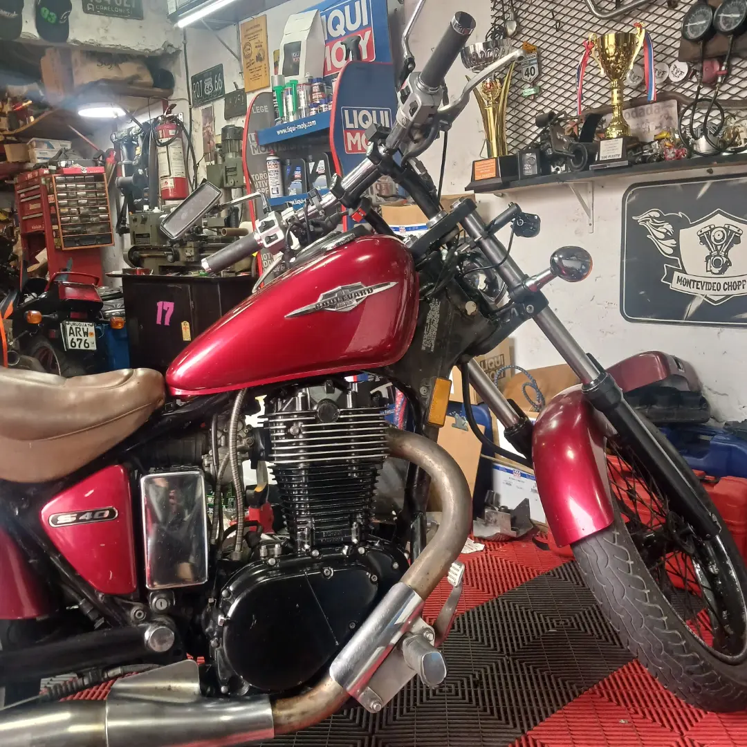 Moto roja dentro del taller Montevideo Choppers, con sus herramientas y emblema al fondo
